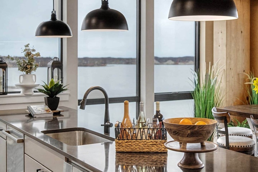 Kitchen island under black dome pendants, with Muskegon Lake filling the windows behind the sink