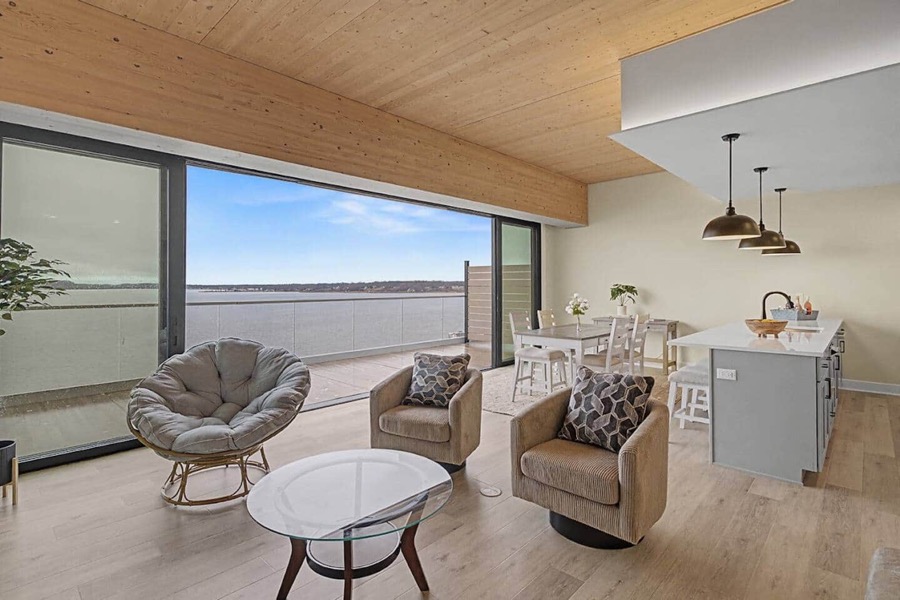 Residence 602's breezy coastal living space — papasan and swivel chairs around a glass table, with the powder-blue kitchen island and open glass wall to the lake-view deck